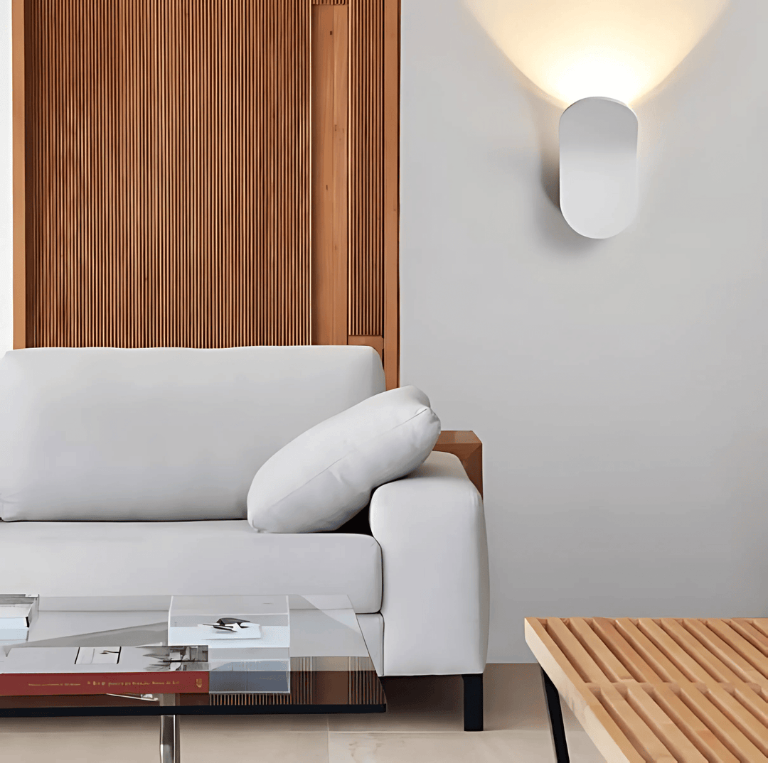 Modern white oval metal wall sconce emitting soft light onto a light grey wall.
