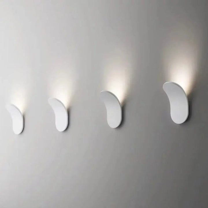 Four modern white metal wall sconces mounted on a gray wall, casting soft light upwards.