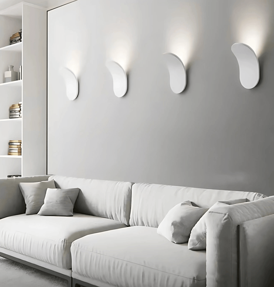 Four modern white metal wall sconces mounted on a grey wall above a white sectional sofa.