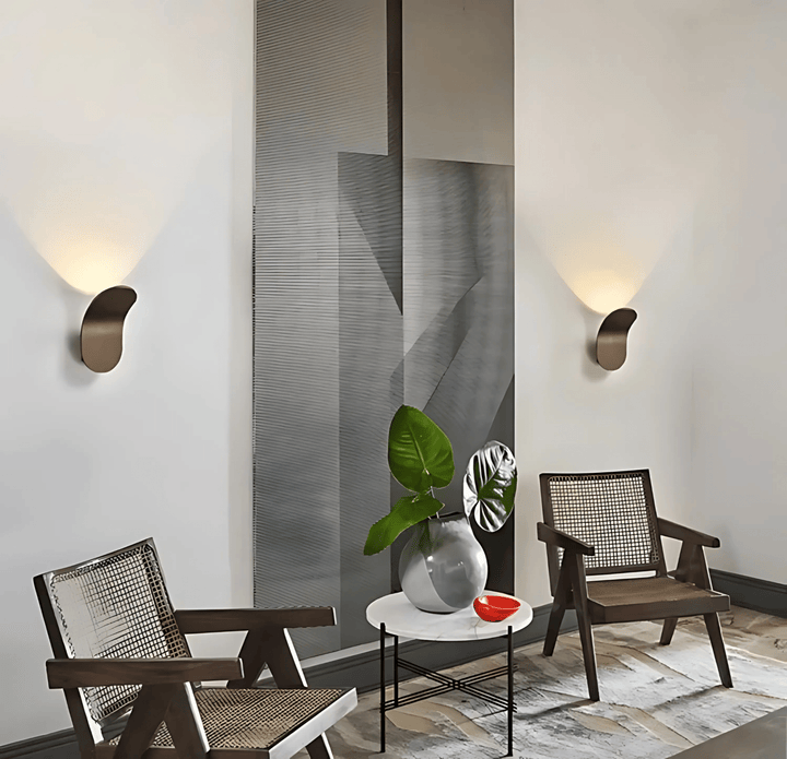 Modern metal wall sconce with a curved, brushed finish, casting a warm light on a white wall.
