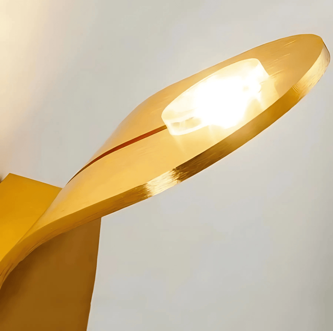Modern metal wall sconce with a curved, golden finish and a lit bulb.