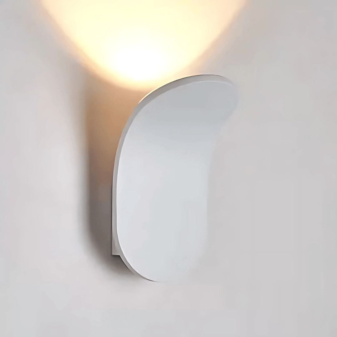 Modern white metal wall sconce with a curved design, casting a warm light upwards.