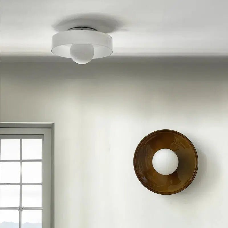 Flush mount ceiling light with a white drum shade and a frosted glass diffuser, and a wall sconce with a bronze bowl and frosted glass diffuser.