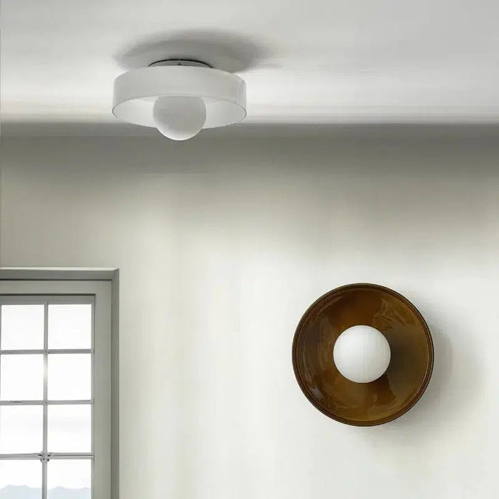 Flush mount ceiling light with a white drum shade and a frosted glass diffuser, and a wall sconce with a bronze bowl and frosted glass diffuser.