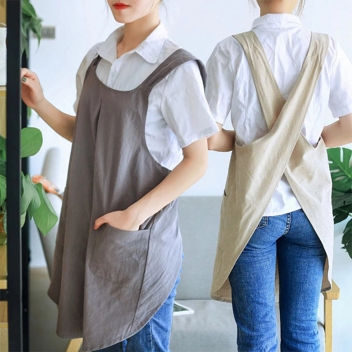 Two women wearing Korean-inspired cross-back linen aprons. One in grey, one in beige.