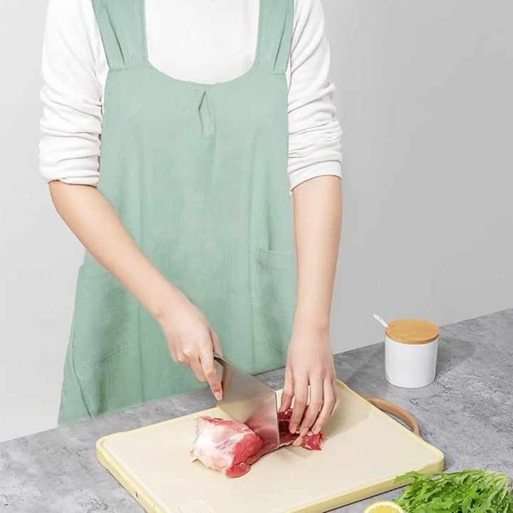 Person wearing a light green linen cross-back apron, chopping meat on a cutting board.