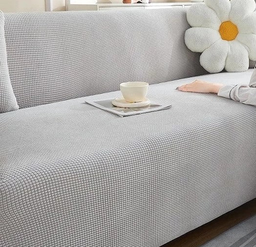 Light grey narrow jacquard couch cover with a textured weave and a white flower pillow.