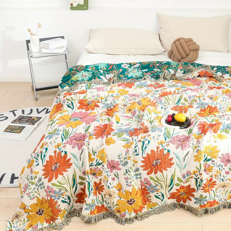 Blooming floral all-season cotton blanket with fringe edges draped over a bed.