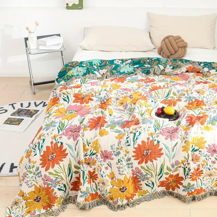 Blooming floral all-season cotton blanket with fringe edges draped over a bed.