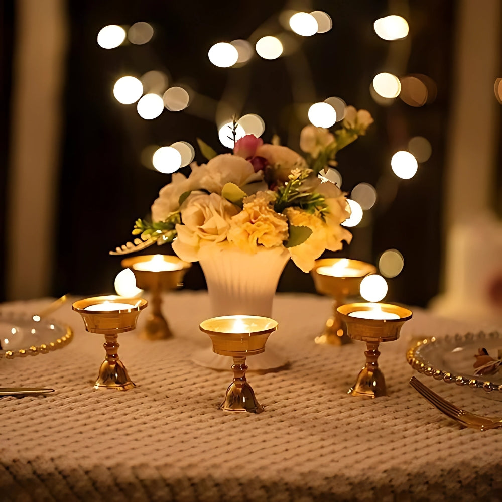 Four vintage copper cup candle holders on a table with a floral arrangement and fairy lights.