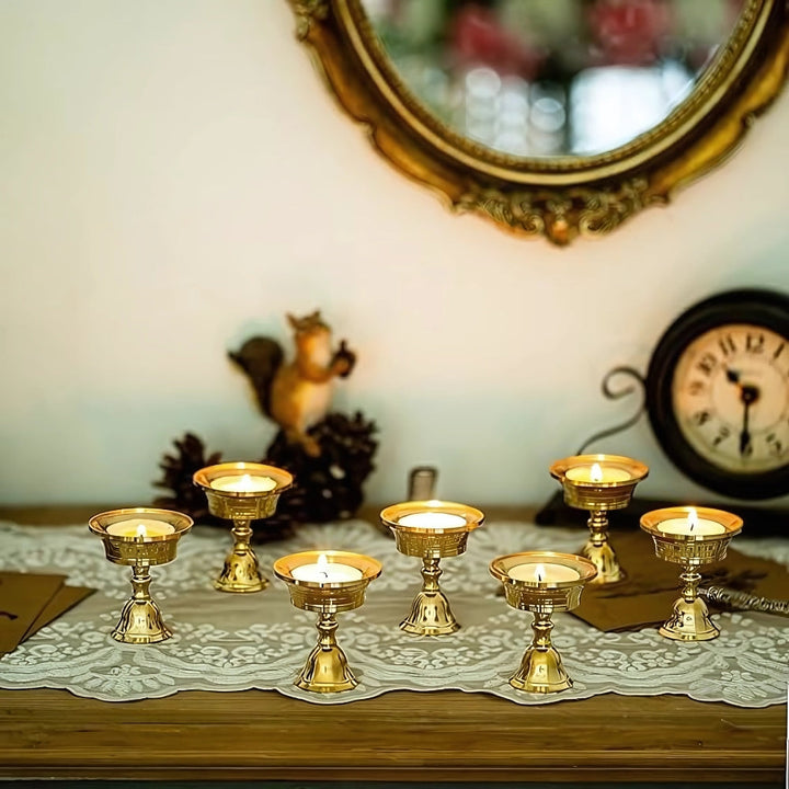 Seven vintage copper cup candle holders with lit candles on a lace runner.