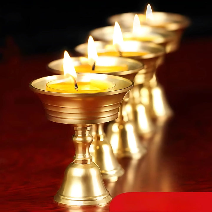 Row of vintage copper cup candle holders with lit yellow candles.