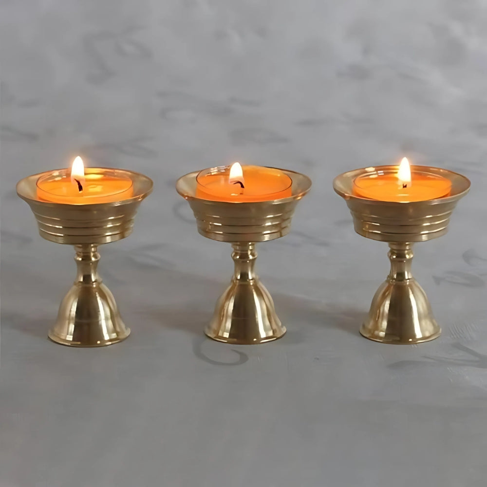 Three vintage copper cup candle holders with lit orange candles.