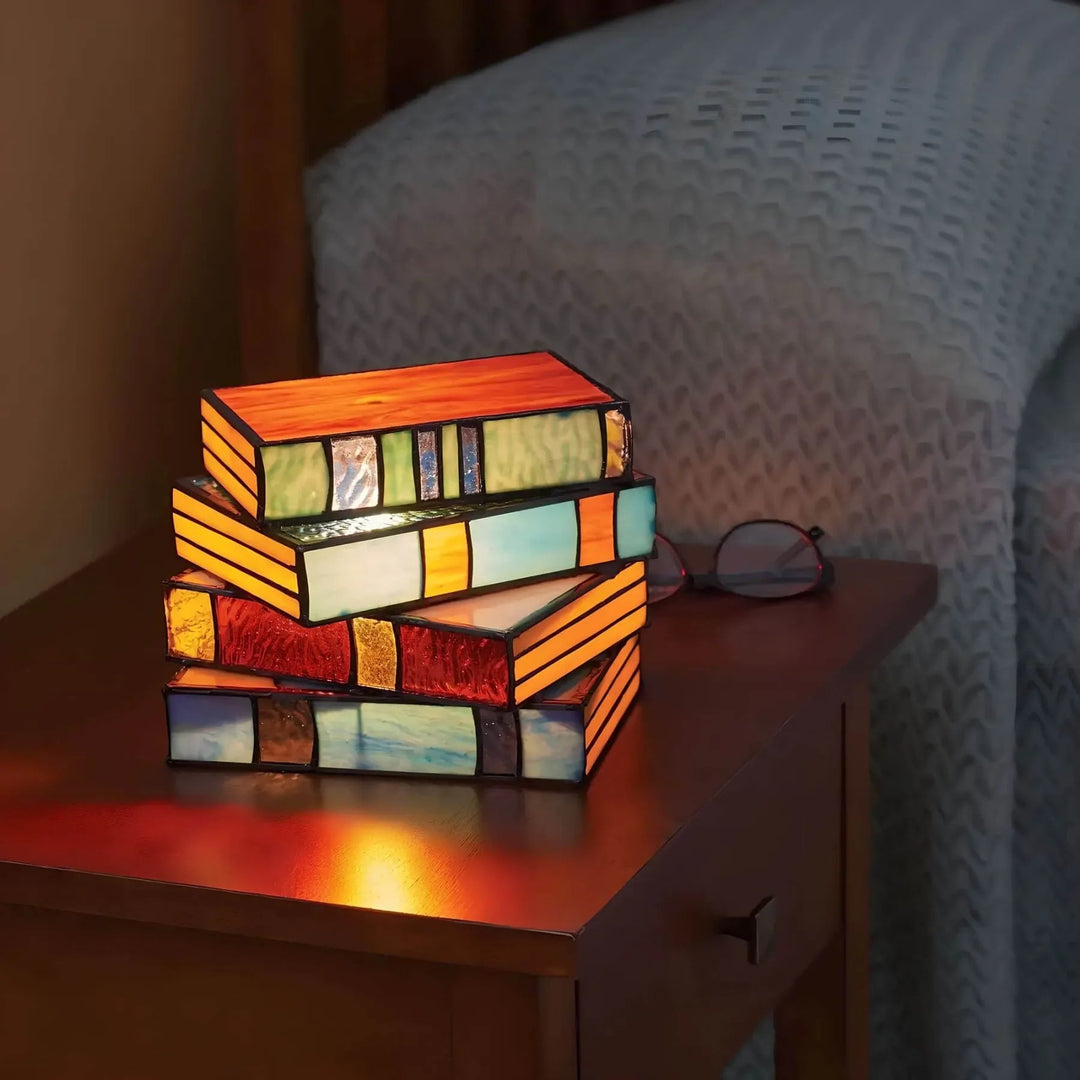 Stack of four stained glass lamps shaped like books, emitting a warm glow.