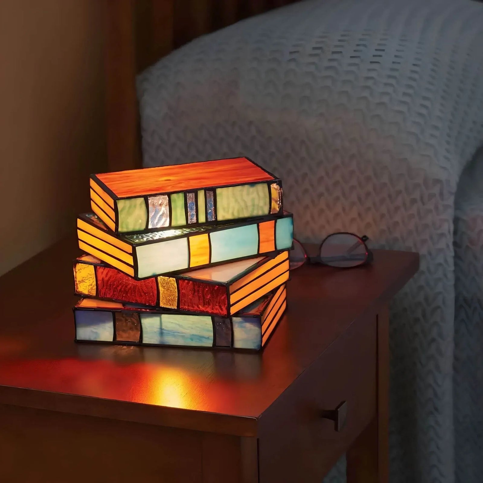 Stack of four stained glass lamps shaped like books, emitting a warm glow.