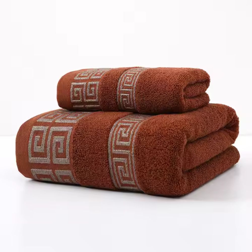 Two rust-colored cotton towels with a Greek key pattern border, stacked on a white surface.