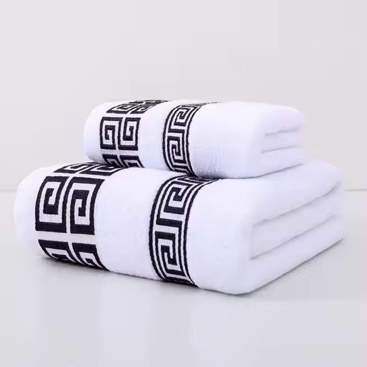 Two white cotton towels with a black Greek key pattern border, stacked on a white surface.