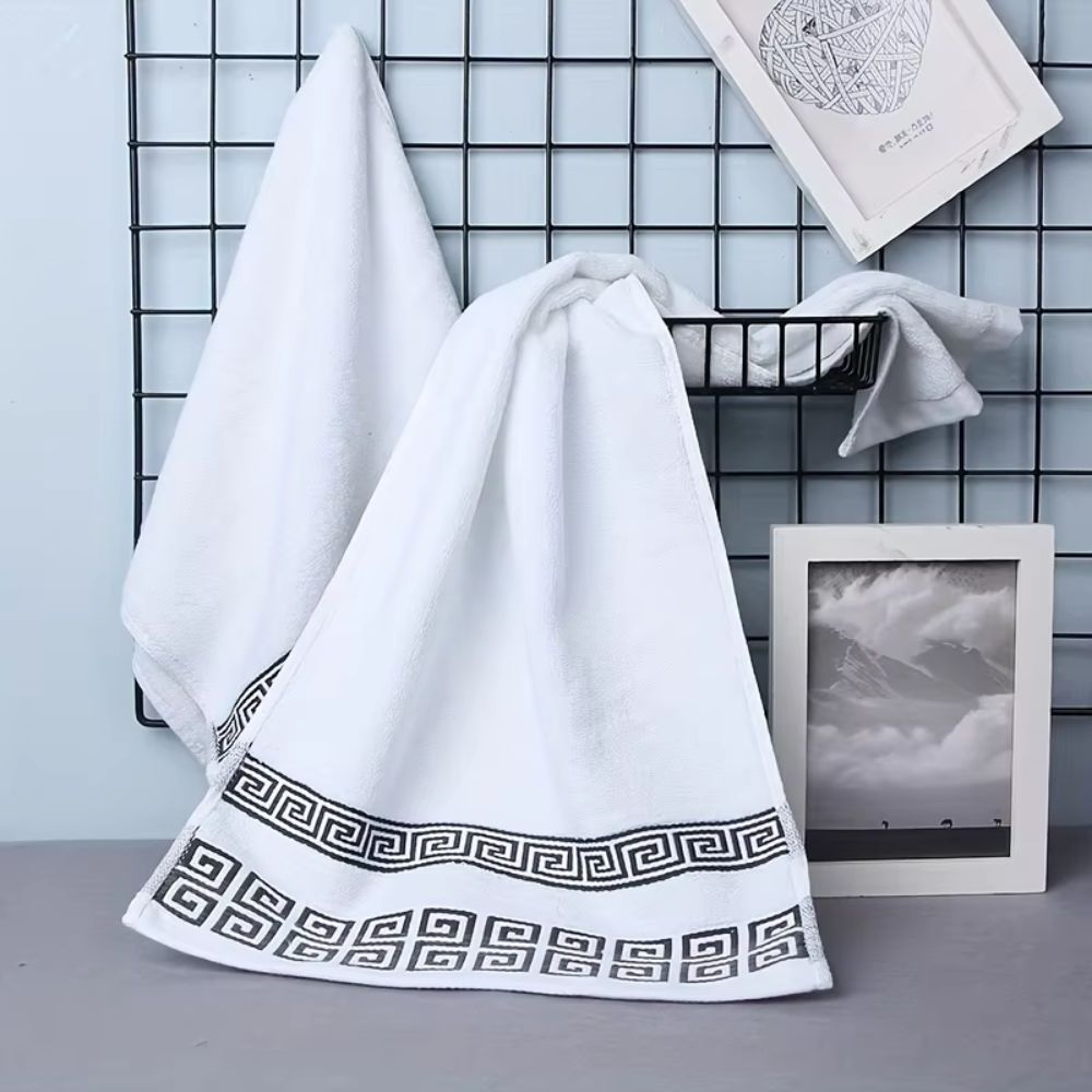 White cotton towel with a black Greek key border hanging on a black rack.