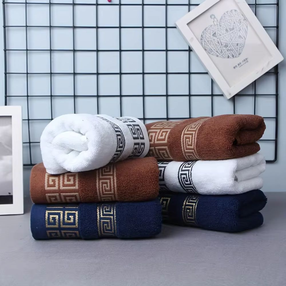 Stack of cotton towels in white, brown, and navy blue with a Greek key pattern.