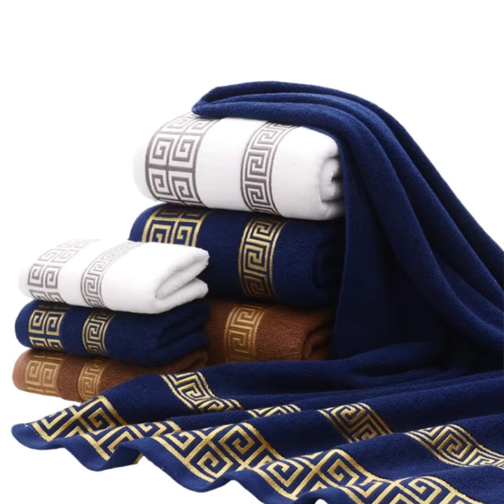 Stack of folded cotton towels in navy blue, white, and brown, with decorative gold and grey Greek key patterns.