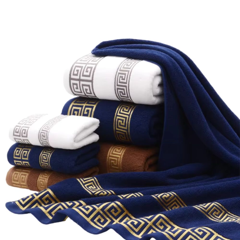 Stack of cotton towels in navy blue, white, and brown with gold Greek key pattern.