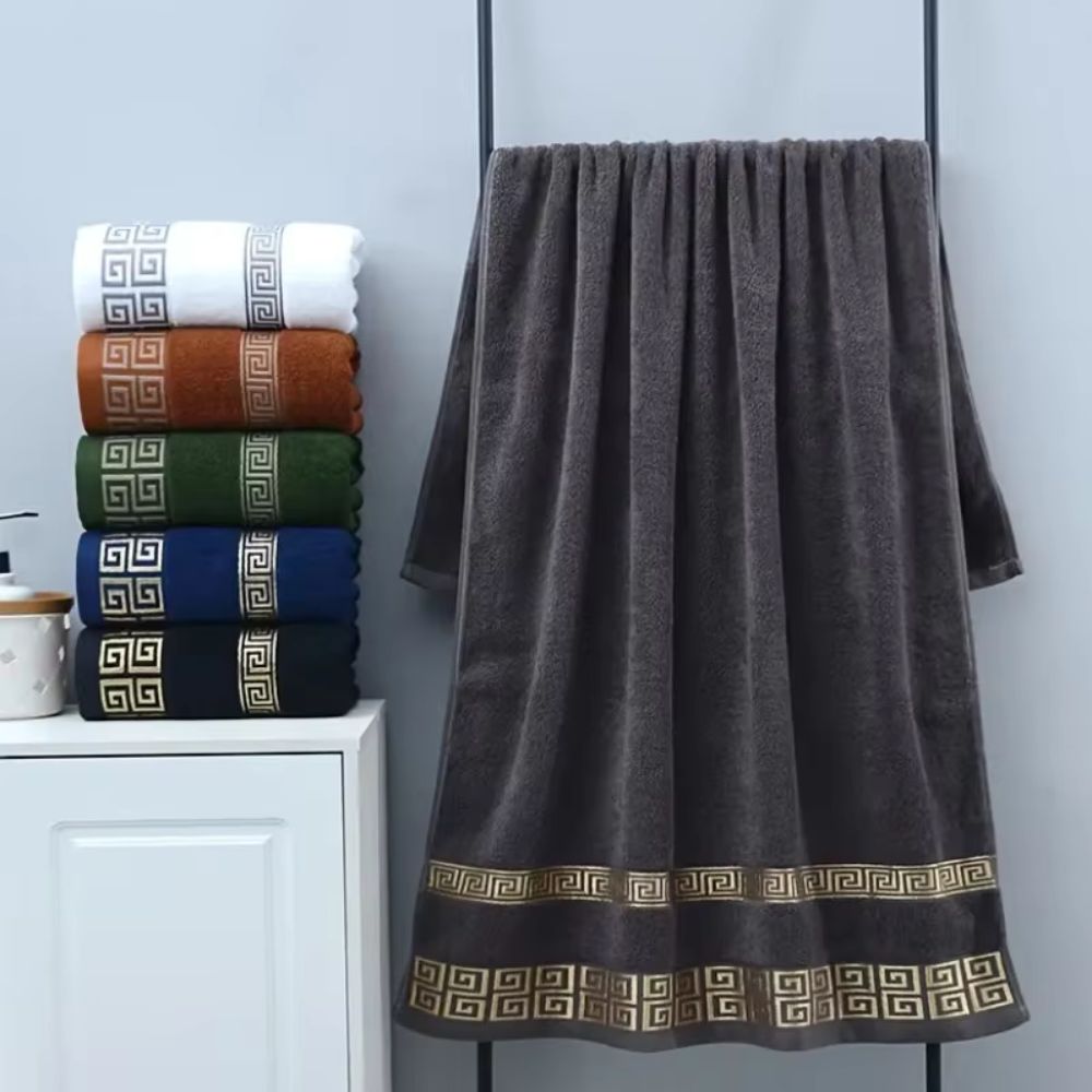 Stack of six cotton towels in white, brown, green, blue, and black, with a large dark gray towel hanging on a rack.