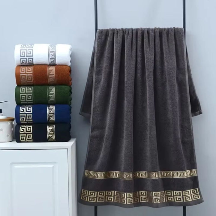 Stack of six cotton towels in white, brown, green, blue, and black, with a large dark gray towel hanging on a rack.
