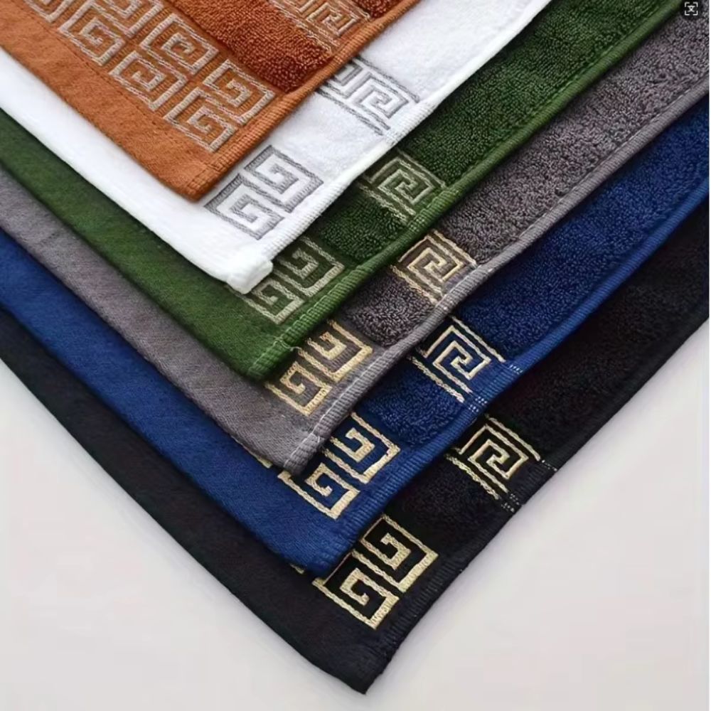 A stack of folded cotton towels in various colors: rust, white, green, gray, navy, and black, each with a Greek key pattern.