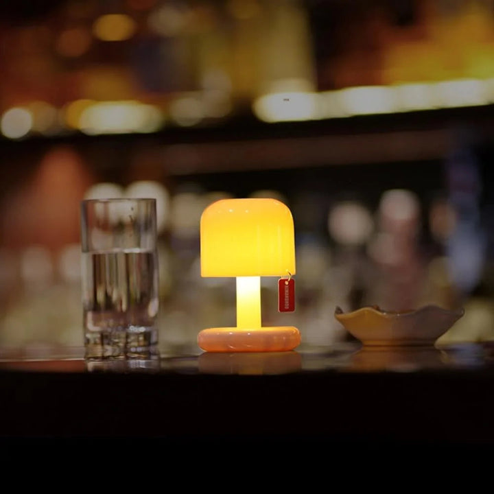 Orange USB rechargeable table lamp with a rounded shade, next to a glass of water.