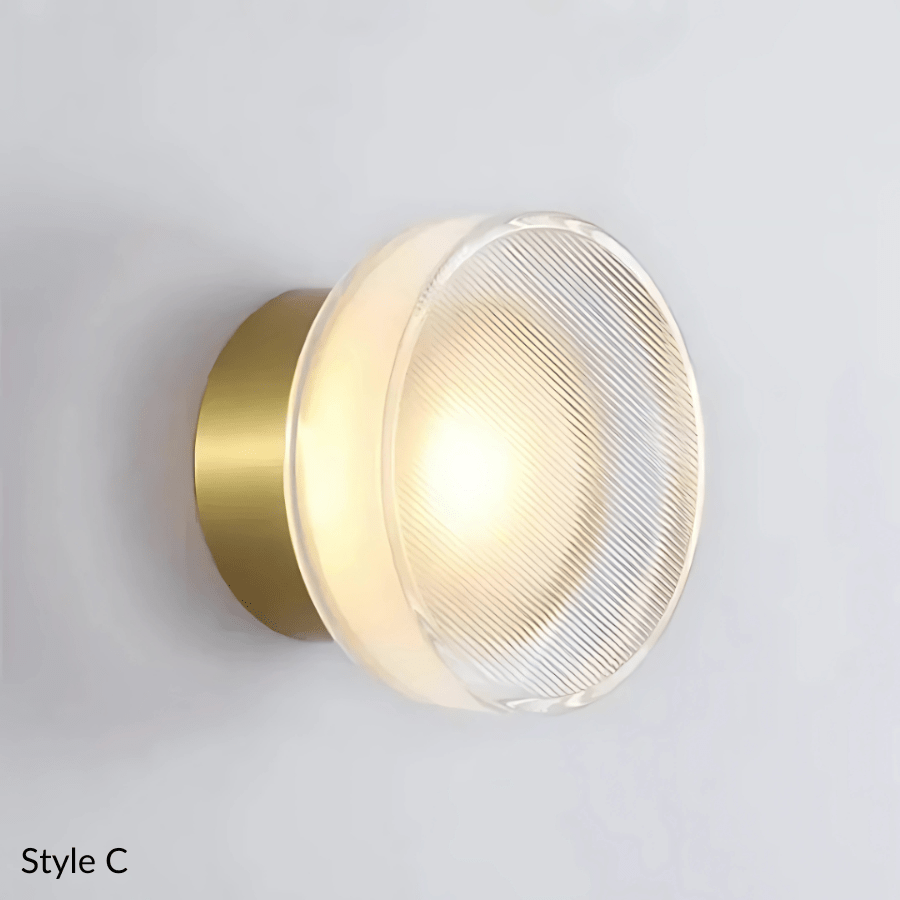 Style C wall sconce with a brass base and a clear, textured glass shade emitting a warm light.
