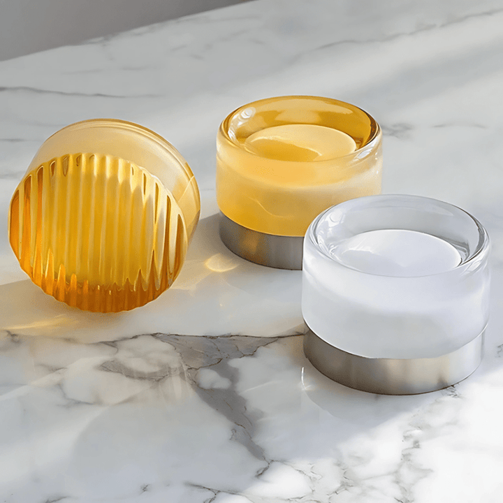 Three cylindrical glass candle holders with metal bases on a marble surface.