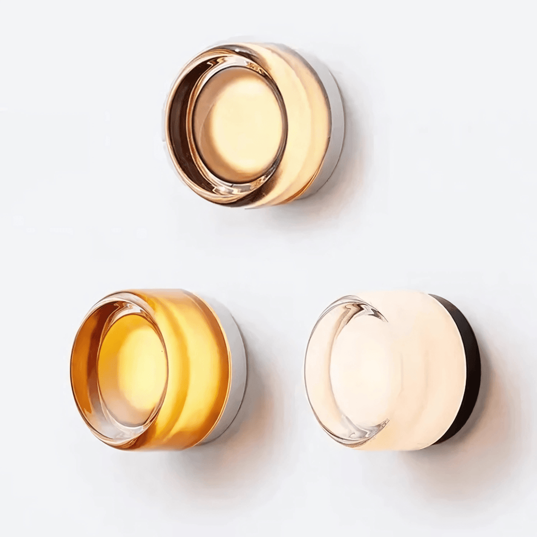 Three modern wall sconces with metal frames and glass shades in amber and clear finishes.