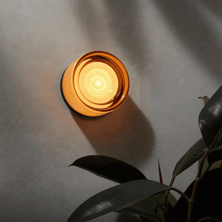 Metal and glass wall sconce with a warm, glowing light against a textured gray wall.