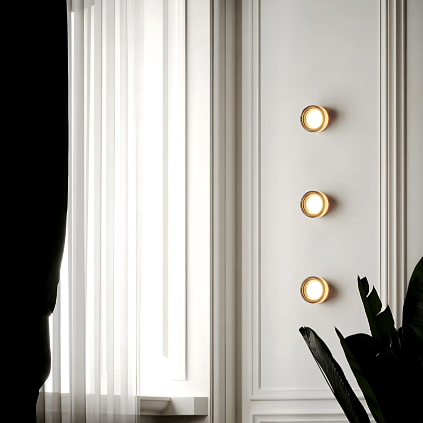 Three round metal and glass wall sconces mounted on a white paneled wall.