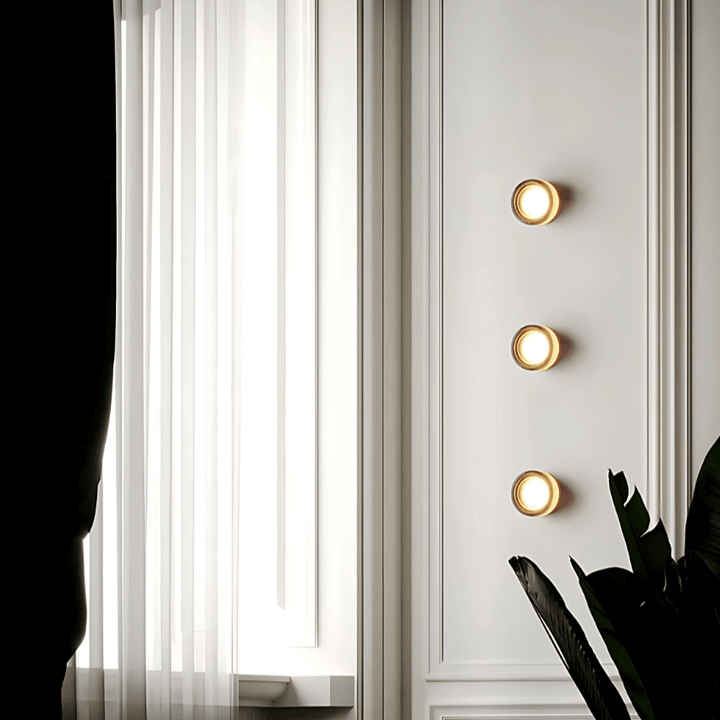 Three round metal and glass wall sconces mounted on a white paneled wall.