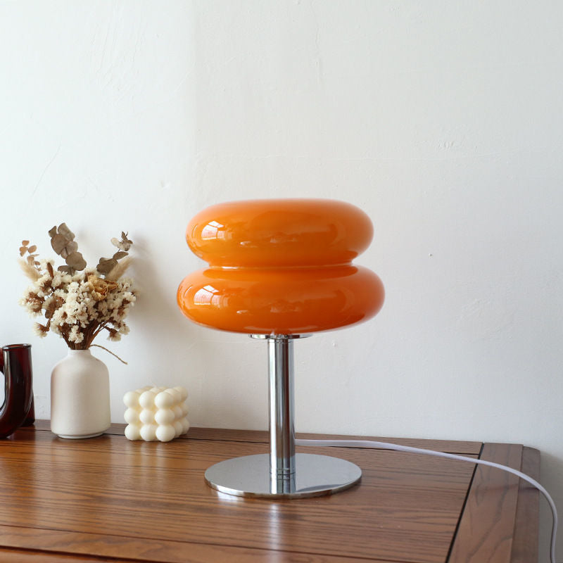 Orange glass retro table lamp with a chrome base on a wooden table.
