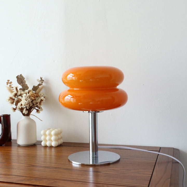 Orange glass retro table lamp with a chrome base on a wooden table.