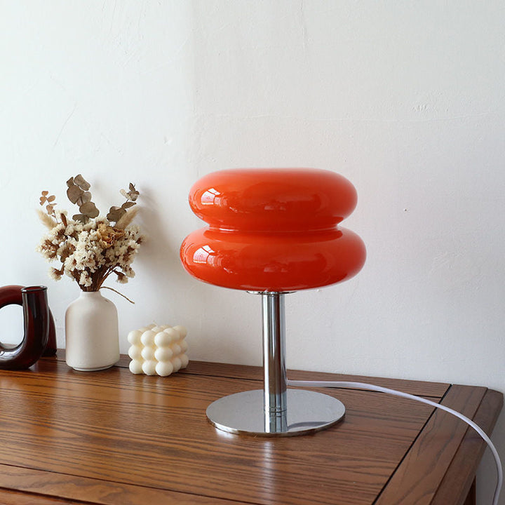 Orange retro glass table lamp with a chrome base on a wooden table.