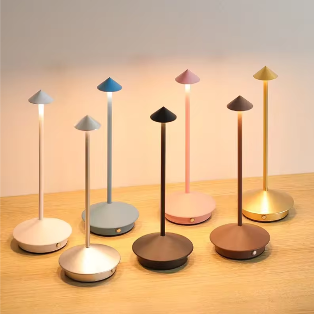 Seven cordless LED table lamps in various colors: white, light gray, blue, black, pink, brown, and gold.