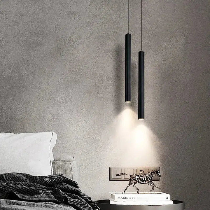 Two black adjustable pendant lights hanging over a nightstand with a book and a horse sculpture.