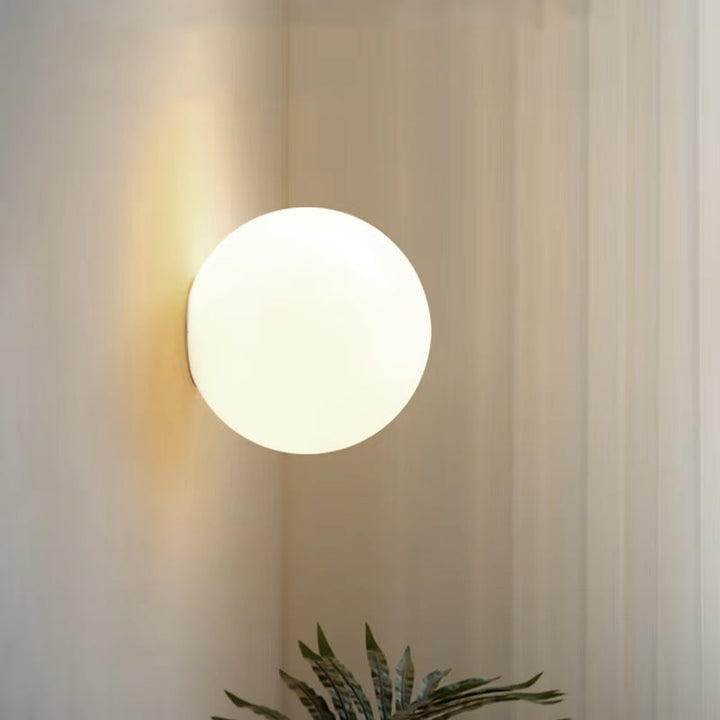 Round frosted glass wall sconce emitting warm ambient light on a neutral wall.