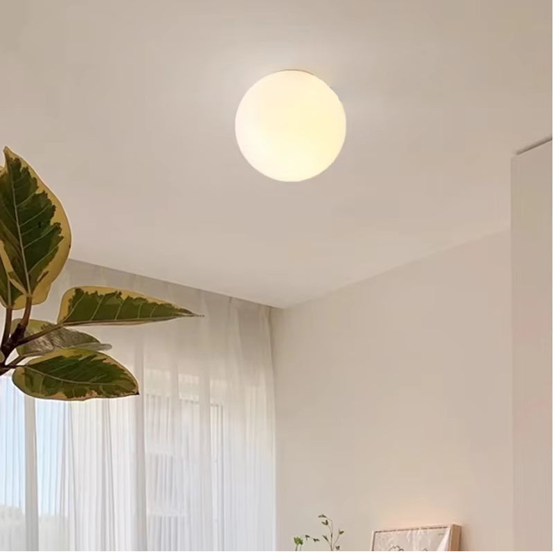 Round glass wall sconce emitting warm light on a white ceiling.