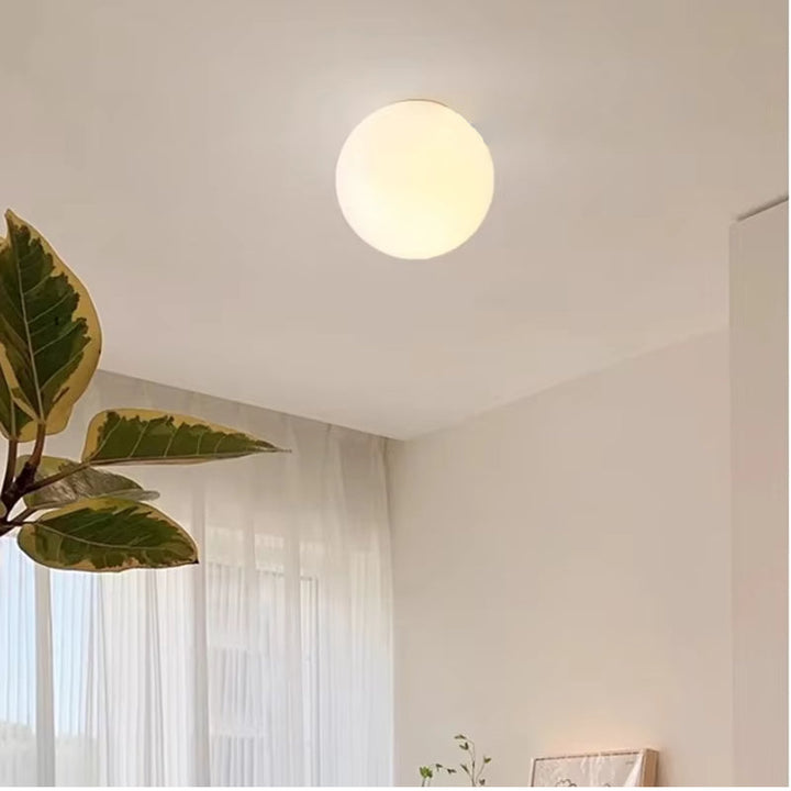 Round glass wall sconce emitting warm light on a white ceiling.