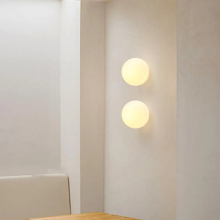 Two round glass wall sconces emitting warm light on a white wall.