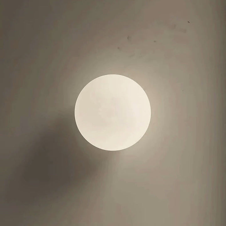 Round glass wall sconce emitting warm ambient light against a neutral wall.