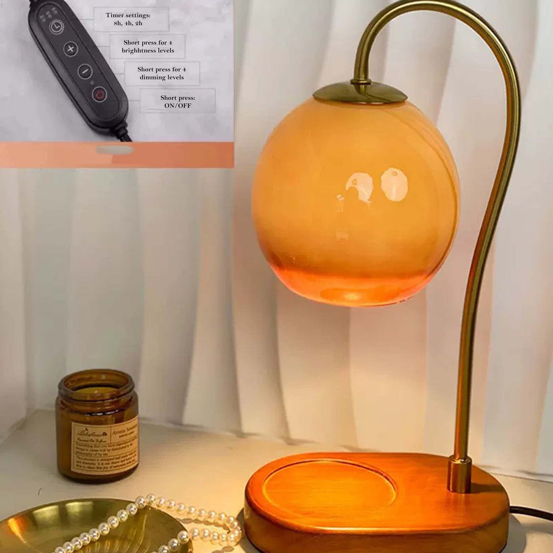 Electric candle warmer lamp with an orange glass shade and a gold curved arm on a wooden base.