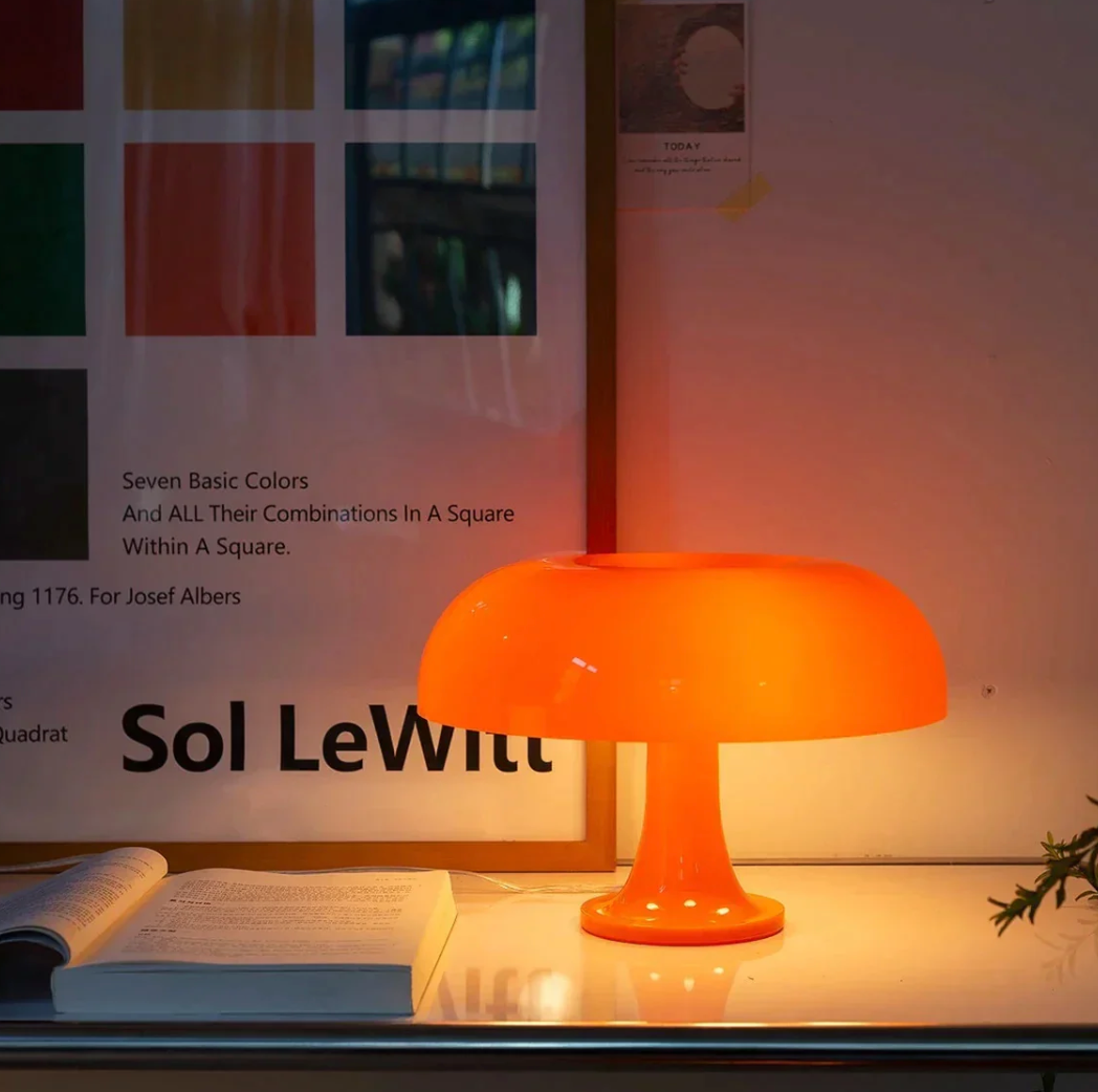 Orange mushroom-shaped LED table lamp emitting a soft glow, placed on a desk next to an open book.