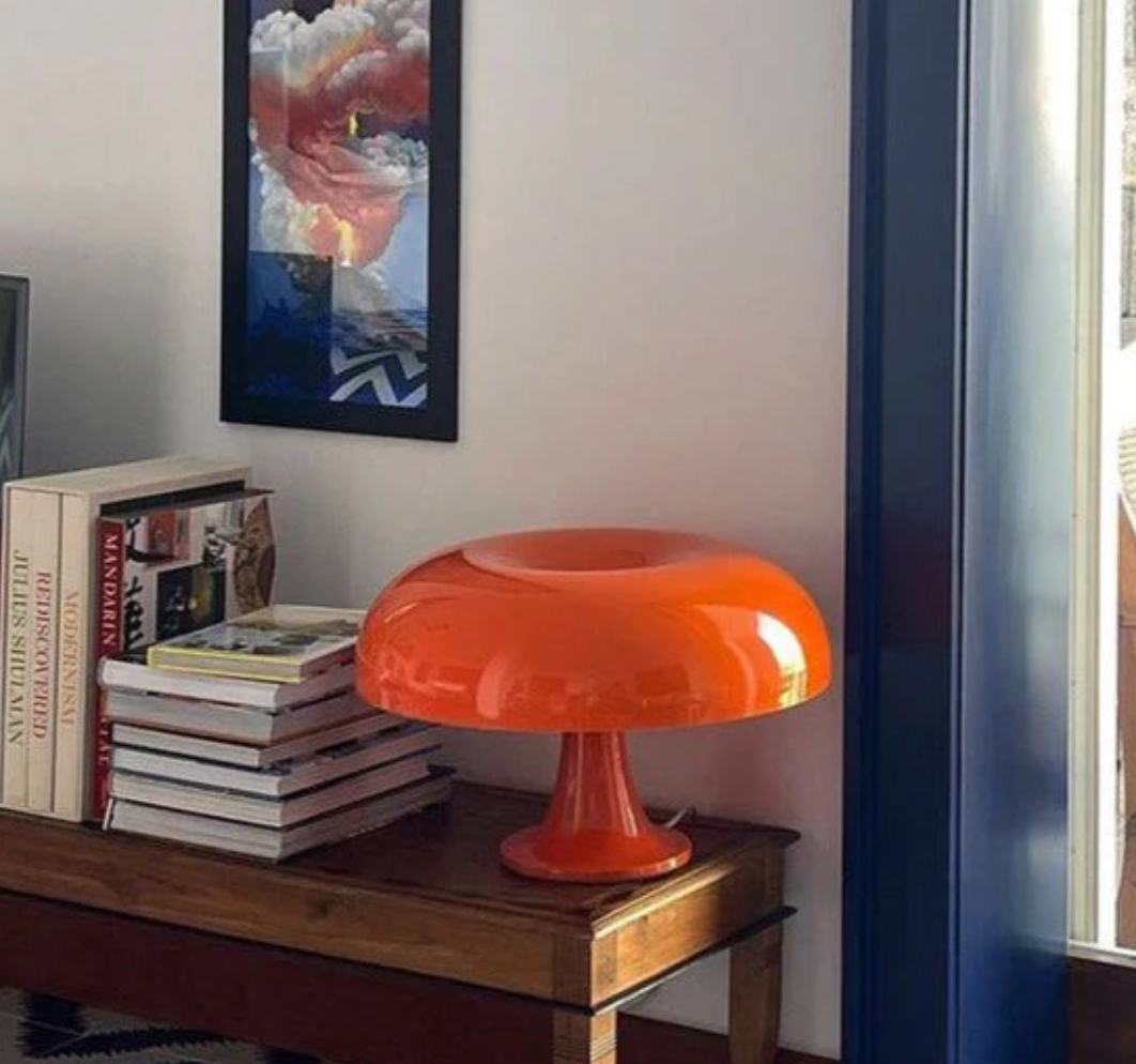 Orange mushroom-shaped LED table lamp on a wooden table with books.