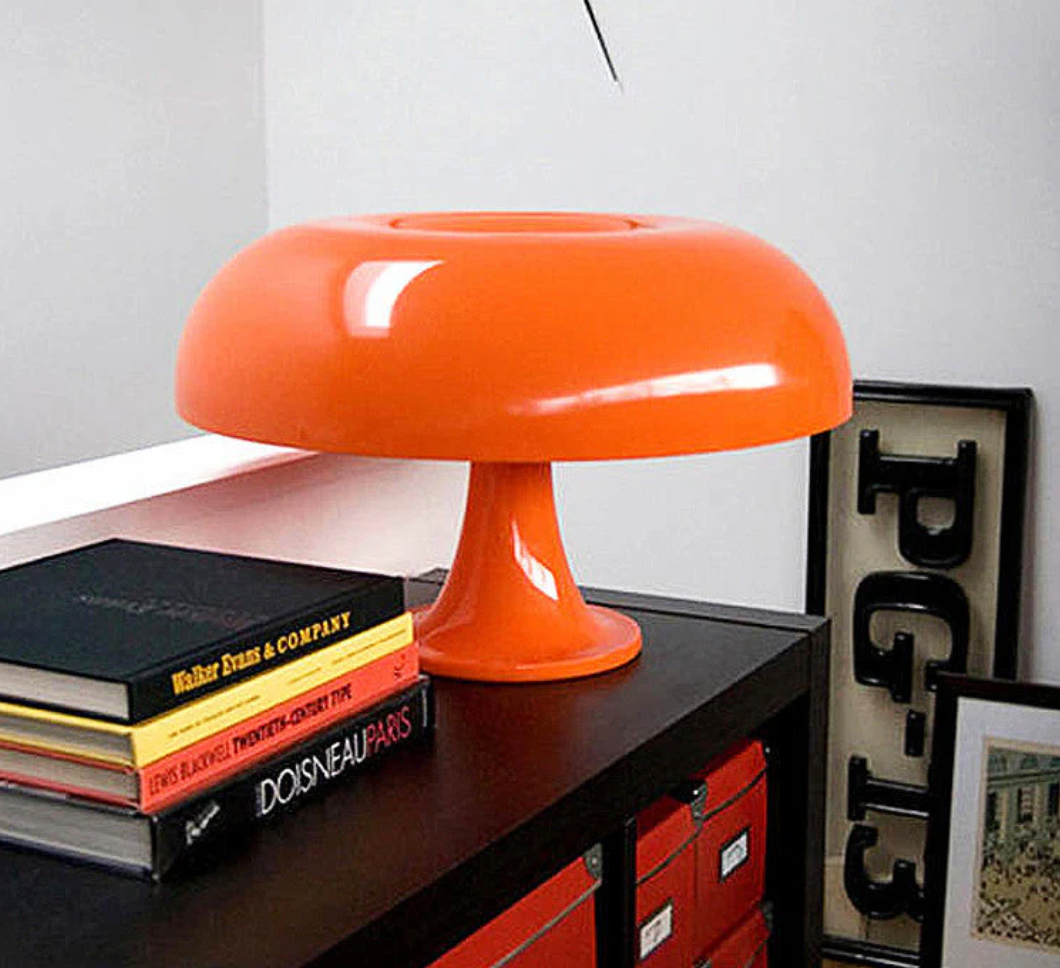 Orange mushroom-shaped LED table lamp on a black shelf with books.