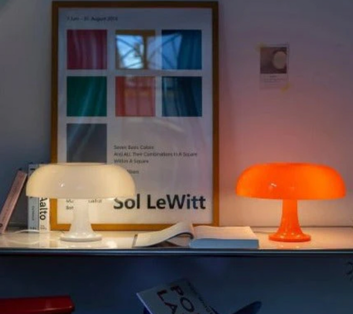 Two mushroom-shaped table lamps, one white and one orange, on a shelf with a poster and books.
